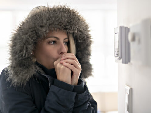 Homeowner in parka looking at thermostat no heat