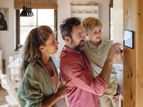 Family looking at smart thermostat, adjusting or lowering heating temperatures at home. Concept of sustainable, efficient, and smart technology in home heating and thermostats.